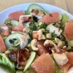 chicken, grapefruit pieces, cucumbers, and cashews over lettuce in the grapefruit grilled chicken salad