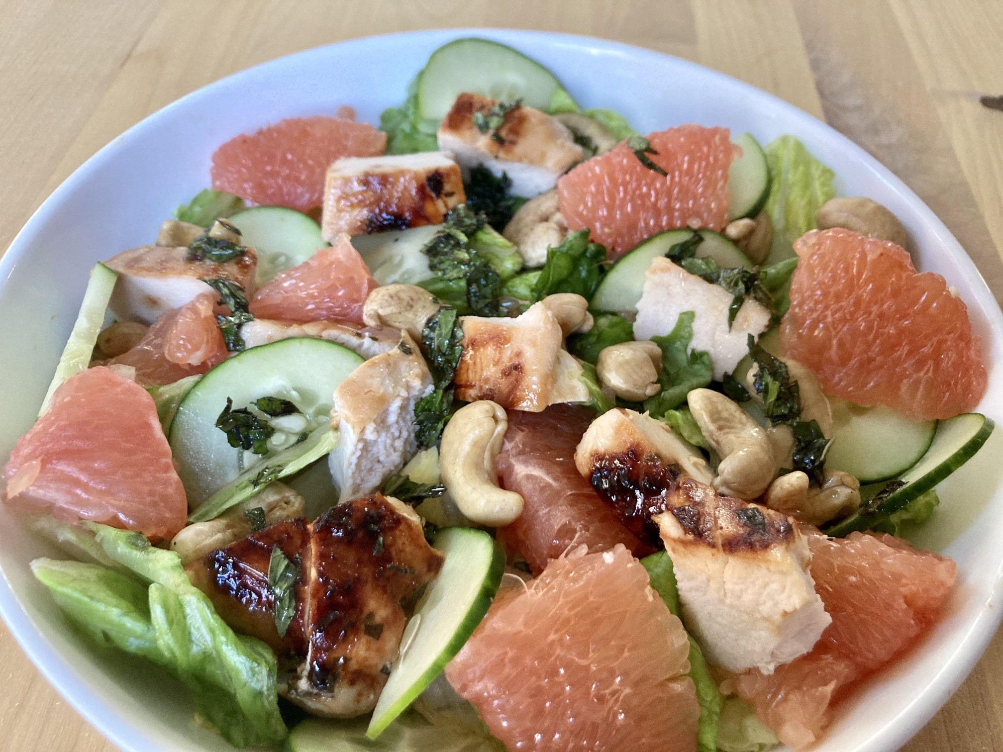 chicken, grapefruit pieces, cucumbers, and cashews over lettuce in the grapefruit grilled chicken salad