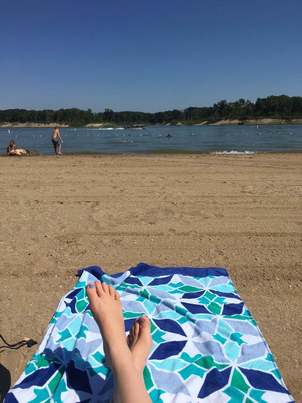 Salamonie Lake beach with kids playing in the water. A woman's feet are shown crossed on a towel in the foreground.