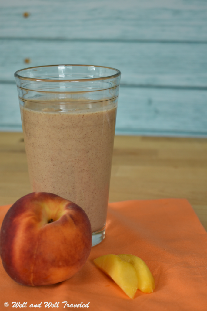 A dairy free peach smoothie in a clear cup with a full peach and peach slices next to it.