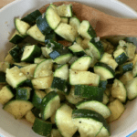 A wooden spoon in the sautéed zucchini side dish bowl