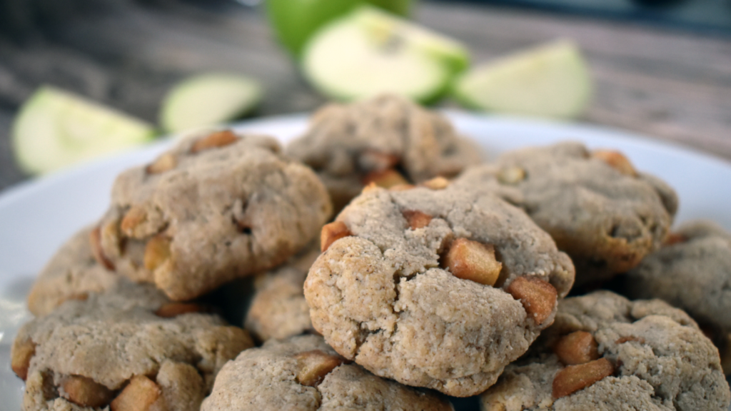 Baked apple cookies with chunks of apple stacked on a plate with green apples in the background.