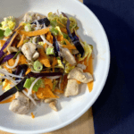 Paleo Pad Thai with chicken, purple cabbage, bean sprouts and carrots in a large white bowl with a navy blue napkin next to it.