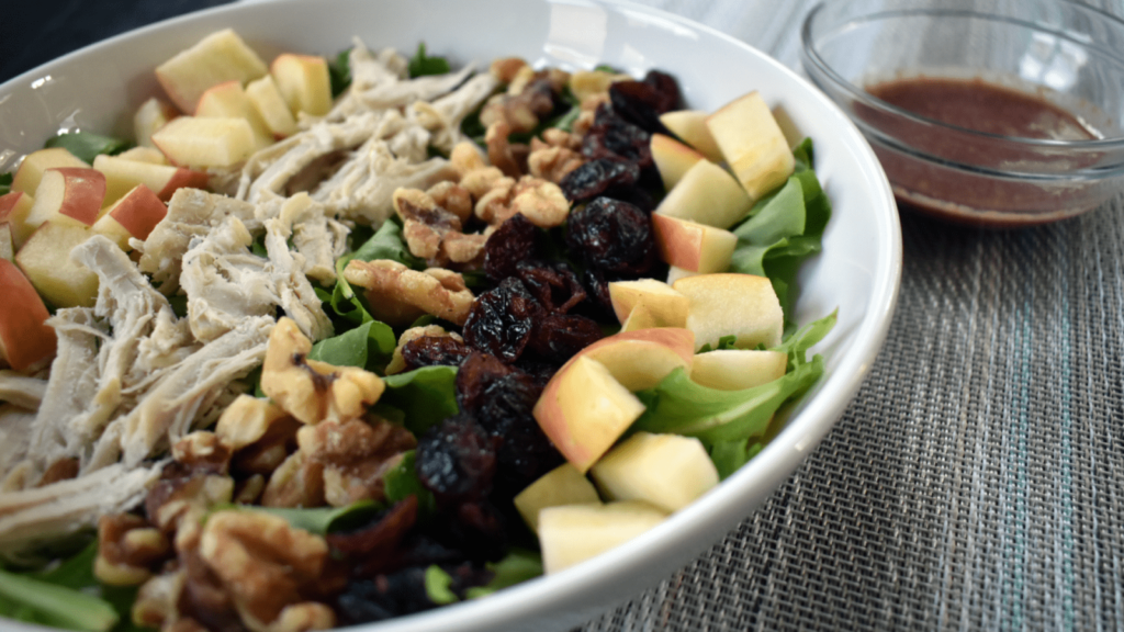 A salad with turkey, cranberries, walnuts, and apples recipe in a white bowl