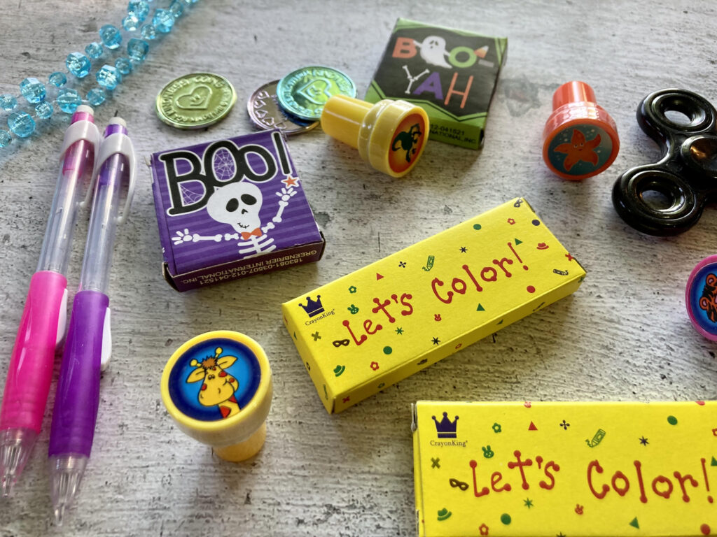 Several Halloween giveaway ideas including stamps, stickers, fidget spinners, pencils, bead necklaces, and even fun coins