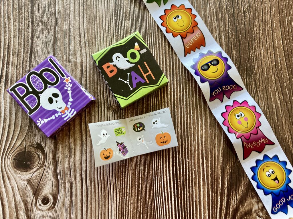 Stickers that are both Halloween and non-Halloween themed on a wood table for a few examples of non-candy Halloween treat ideas