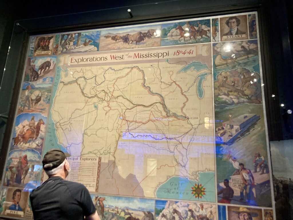 A man standing in front of a huge poster that says "Explorations West of the Mississippi"