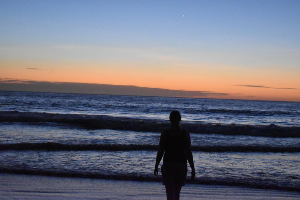 The siloette of a woman in front of the ocean with the sun setting.