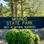 A sign made from stone and wood that says "Mounds State Park"