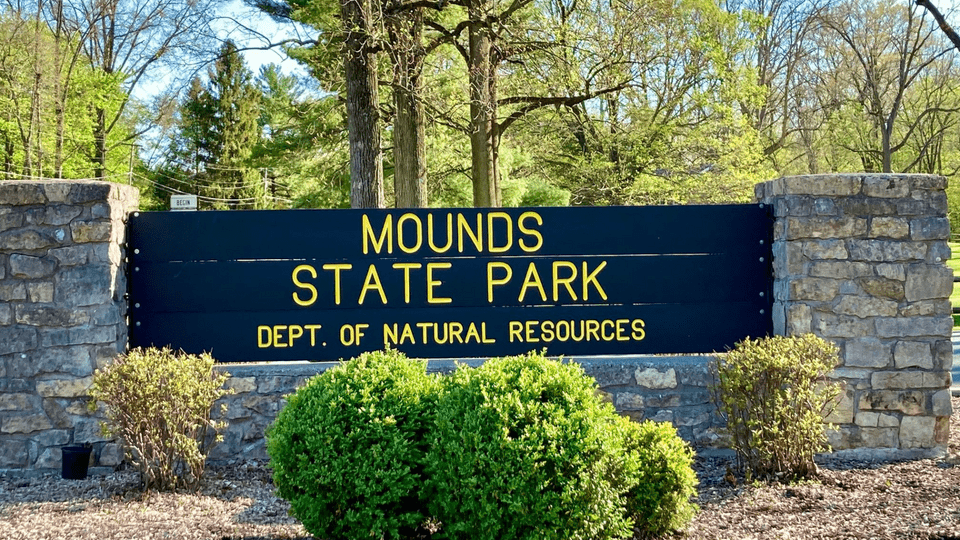 A sign made from stone and wood that says "Mounds State Park"