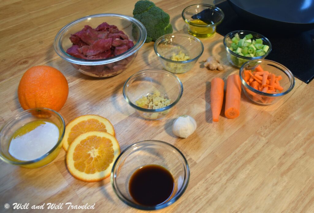A wooden table with orange slices, beef, carrots, broccoli and more