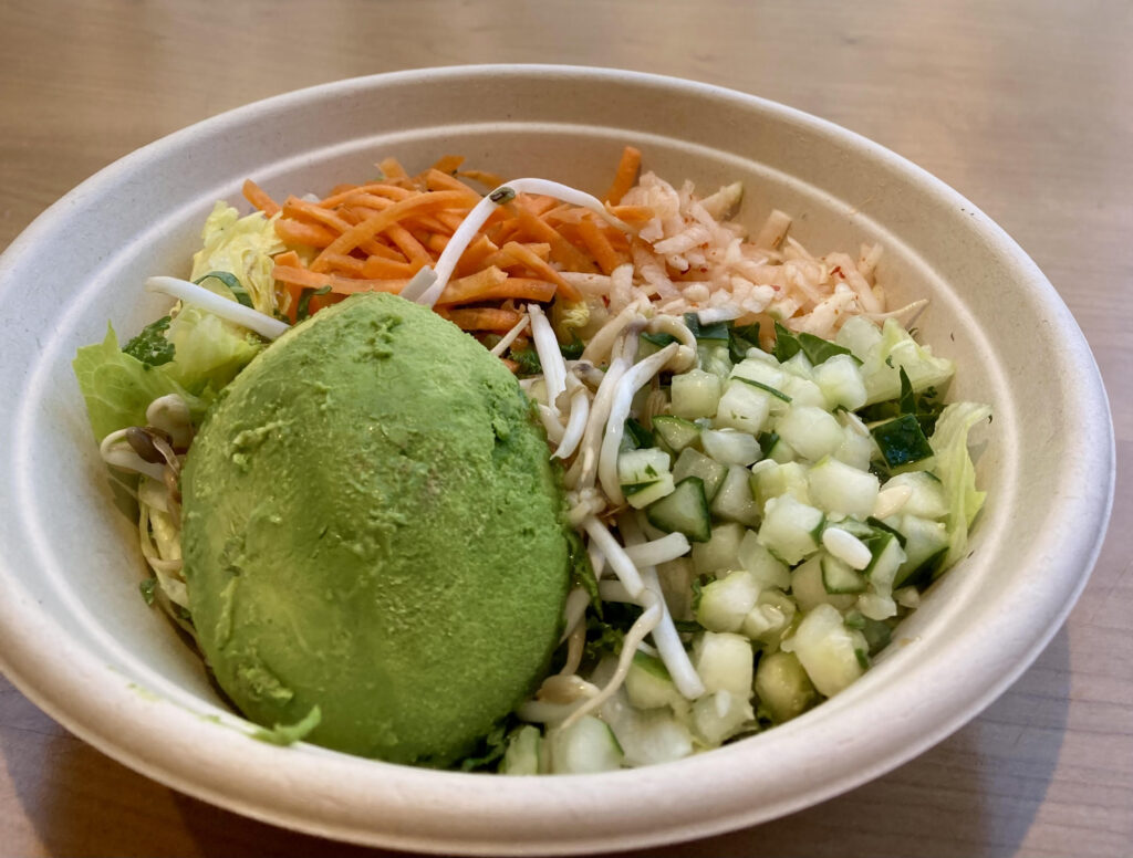 A bowl with cucumbers, carrots, slaw, avocado and more