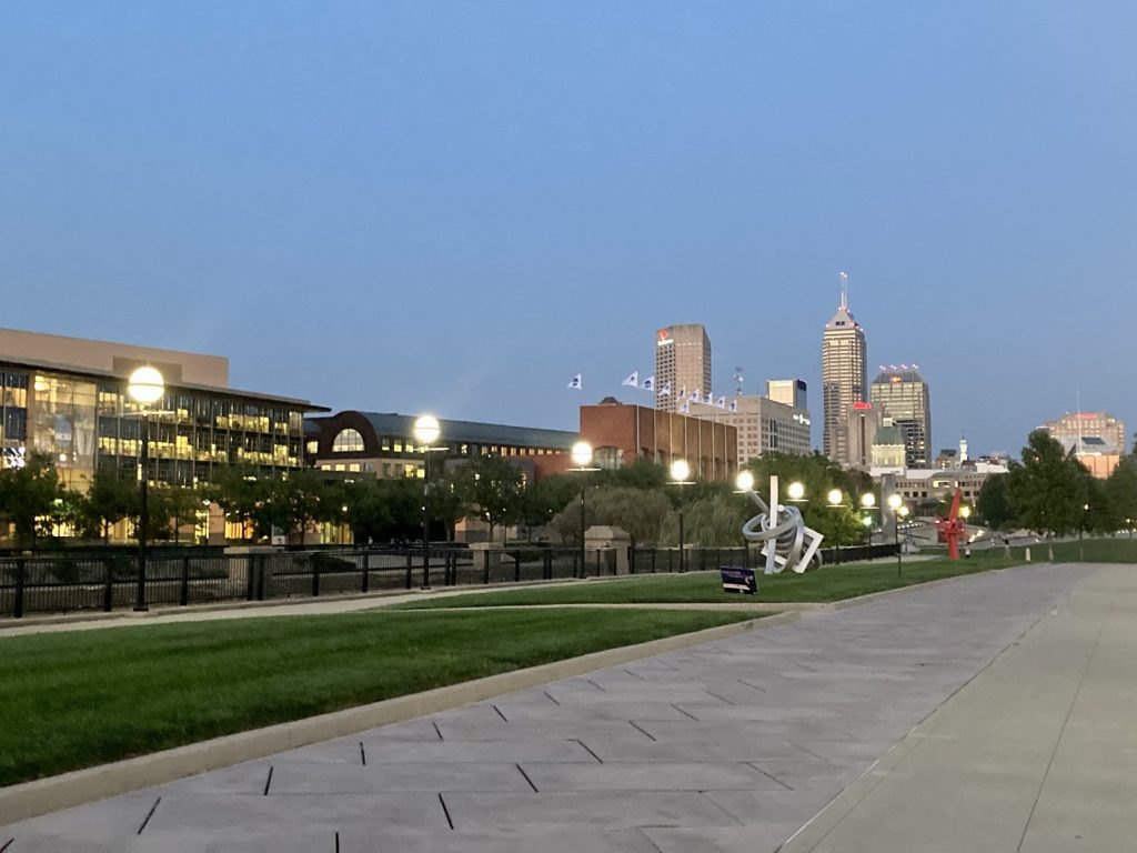 A grassy area with art sculptures in the front and the skyline of Indianapolis in the background