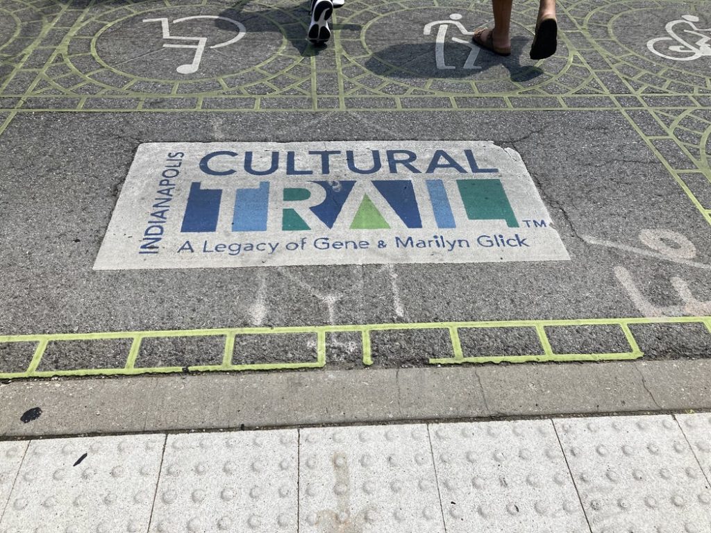 Two sets of feet walking over a painted sign on the ground that says "Cultural Trail" in Indianapolis