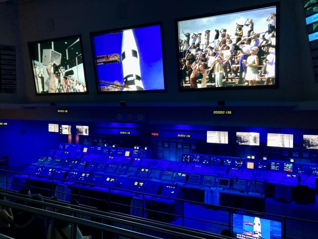 A video displayed on the screen above with a mission control center below at the Apollo/ Saturn V Center on the NASA bus tour