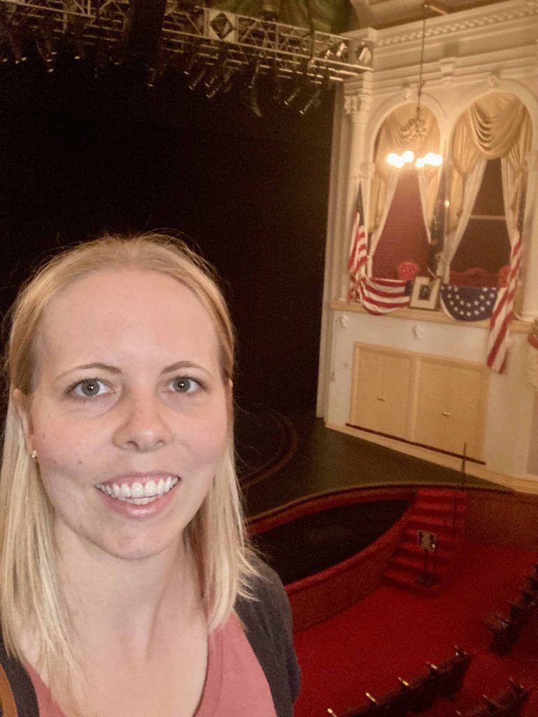 A woman standing in Ford's Theatre on the Ford's Theatre tour Washington D.C. with the presidential box in the background.