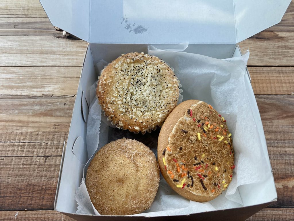 A gluten-free and dairy-free poppyseed muffin and cakie next to a gluten-free donut muffin in a box to go.