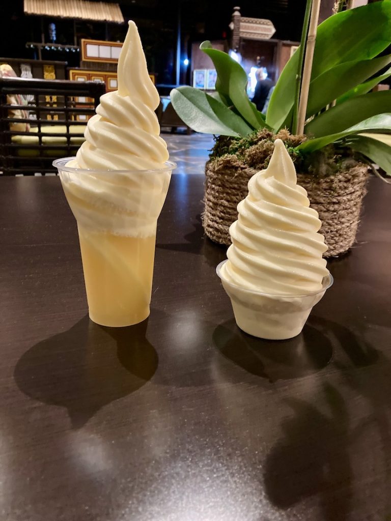 Two DOLE Whips, one in a cup and one as a float with pineapple juice. An orchid is in the background